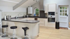 Eine moderne Küche mit einer zentralen Kochinsel, Barhocker, einem eingebauten Backofen und weißen Schränken.