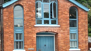 Ein roter Backsteinbau mit blauer Tür und Fenstern, mit der Aufschrift "St. Monica's".