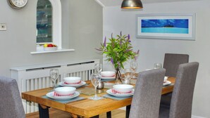 Ein Essbereich mit einem Holztisch, gedeckter für vier Personen, grauen Polsterstühlen, einem Topf mit Pflanze und einem gerahmten Bild an der Wand.