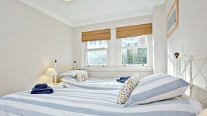 A bedroom with two beds, a window with a view of trees, and a bedside table with a lamp. - 3 bedroom accommodation in Fowey (Fowey)