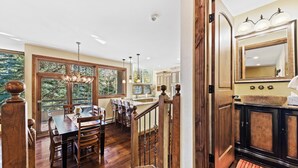 Un vaste espace dédié à la salle à manger, avec une table et des chaises en bois, un escalier menant à une cuisine équipée de meubles en bois et d’un grand miroir au-dessus de l’évier.