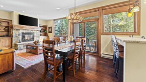Une cuisine spacieuse avec une cheminée en pierre, une table à manger en bois et de grandes fenêtres offrant une vue sur l’extérieur.