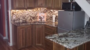 A kitchen with wooden cabinets, a granite countertop, a microwave, and a refrigerator. - Hideaway  by the Sea (Montego Bay)