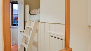 Une chambre avec un lit superposé, une échelle, une fenêtre donnant sur les arbres et une porte menant à une autre pièce.