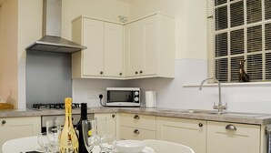 Une cuisine avec des meubles blancs, un four à micro-ondes, une cuisinière à gaz et un évier.