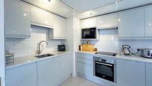 A modern kitchen with white cabinets, a stainless steel sink, a Bosch oven, and a microwave. - 2 bedroom accommodation in Fowey (Fowey)