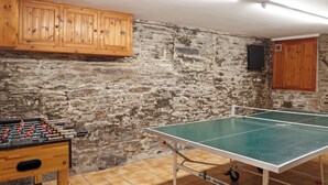 A room with a foosball table, a ping pong table, stone walls, wooden cabinets, and a tiled floor. - 2 bedroom accommodation in Fowey (Fowey)