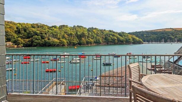 A balcony with a view of a lake, boats, and a forested hillside. - 2 bedroom accommodation in Fowey (Fowey)