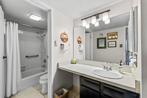 Ein modernes Badezimmer mit Badewanne, Toilette und Waschbecken. Es gibt einen großen Spiegel, einen wandmontierten Handtuchhalter und eine kleine Mülltonne.