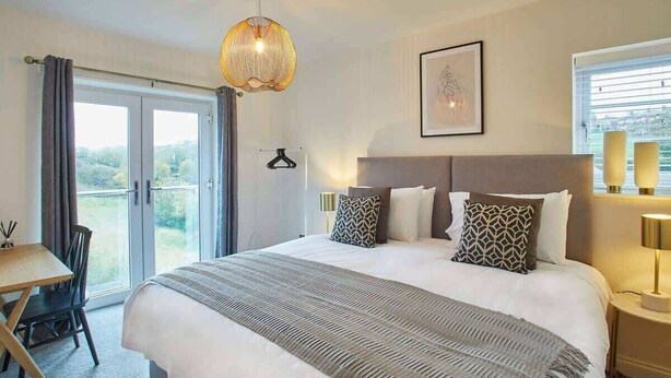 A modern hotel room with a large bed, a desk, and a view of the outdoors.