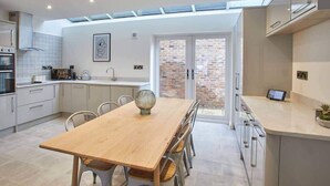 A modern kitchen with a dining area, featuring a wooden table, chairs, and a large window with a view of a brick wall.