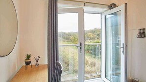 A room with a large sliding glass door leading to a balcony with a view of trees and buildings.