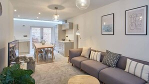 A modern living room with a grey sofa, a round wooden coffee table, and a dining area with a table and chairs.