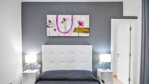 Et moderne soveværelse med en stor seng, to sengeborde med lamper, en hvid sengegavl og et blomstermotiv på væggen.