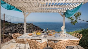 Ein überdachter Essbereich im Freien mit Tisch für zwei Personen mit Blick auf das Meer.