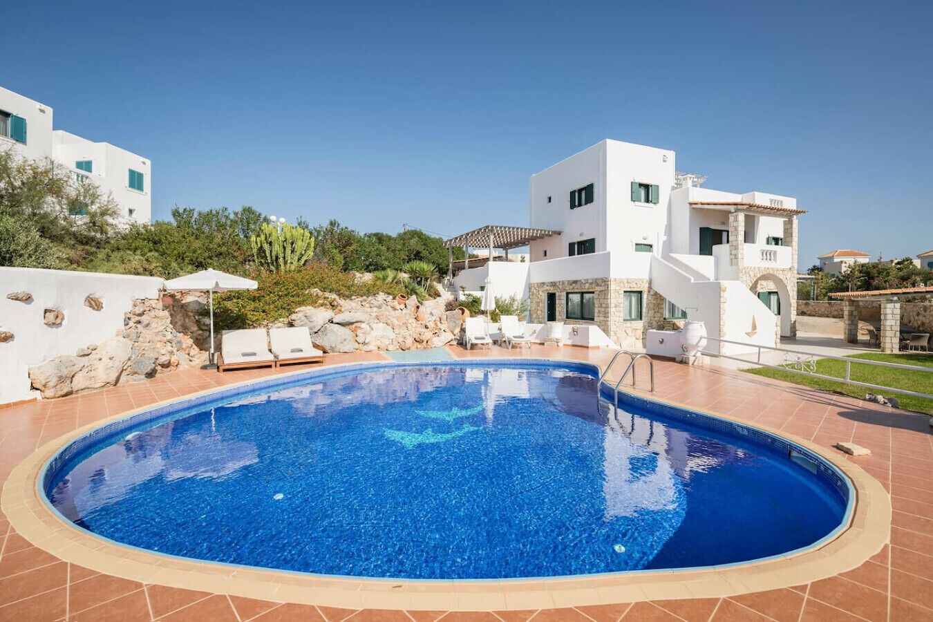 A swimming pool with lounge chairs, a stone wall, and a white building with multiple windows.