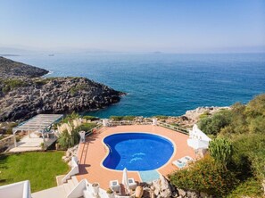 A pool with a curved edge, surrounded by a patio area with chairs and a small deck. - Luxury villa near Beach, with Private Pool & Views (Chania)