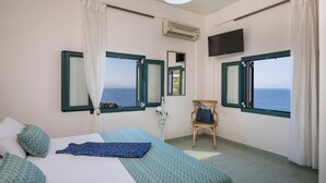 Ein Hotelzimmer mit einem Bett, zwei Fenstern mit Meerblick, einem Sessel und einem Fernseher.