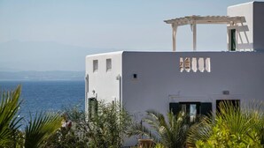 Ein weißes Gebäude mit einer Pergola, Blick auf das Meer und tropischer Vegetation.