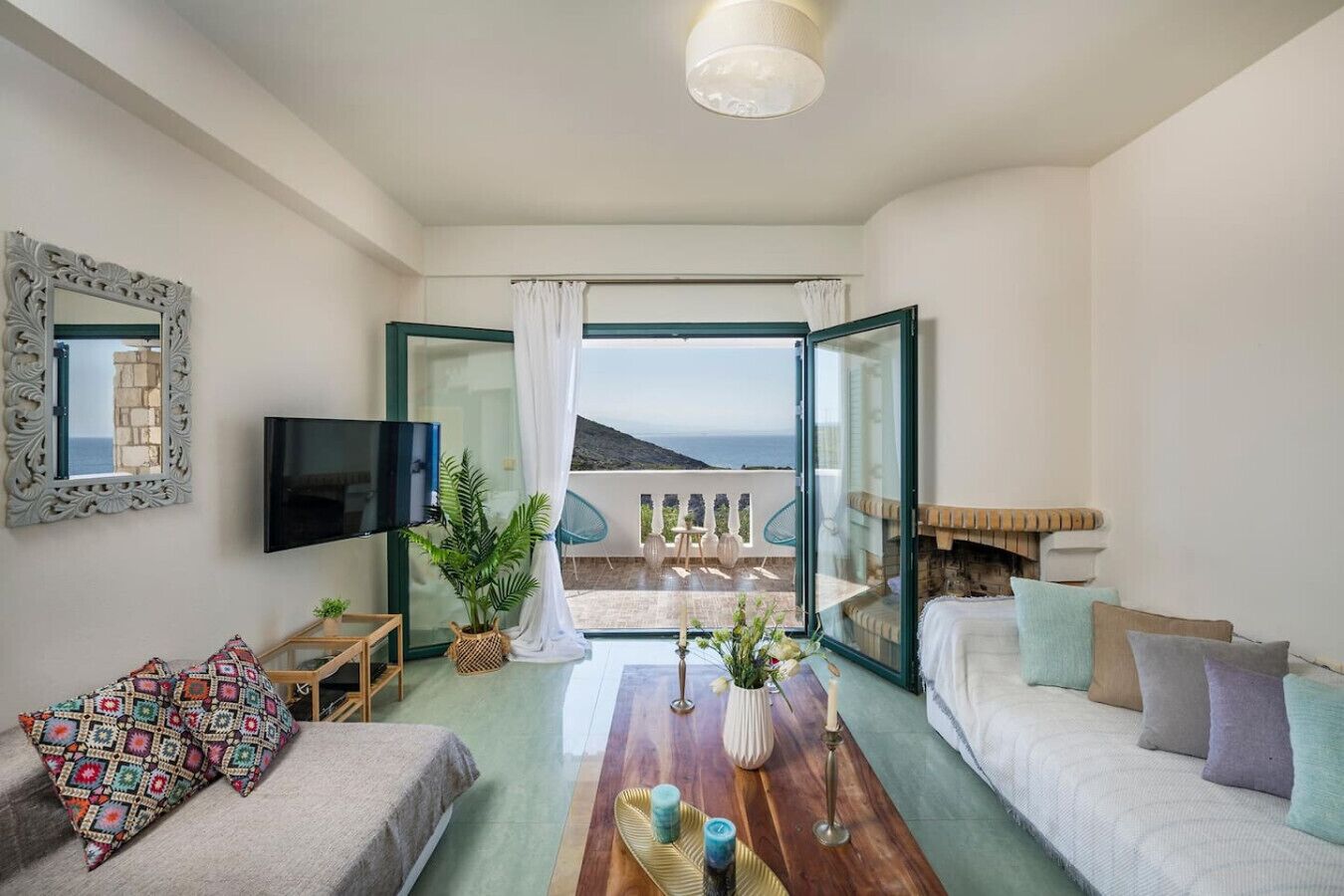 Uma sala de estar moderna com televisão, sofá, mesa de centro e vista para o mar através de uma porta aberta.