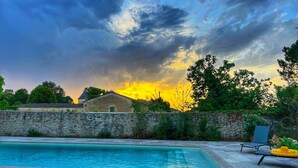 A swimming pool with stone tiles, a stone wall, and a chair with a cushion.