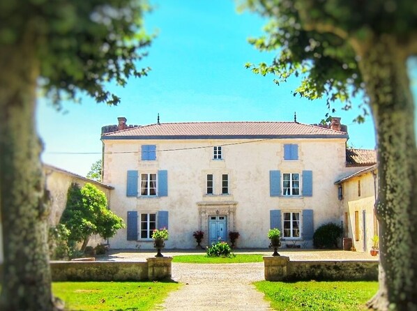 A two-story building with a symmetrical facade, a central entrance with a door, and a small garden area in front.