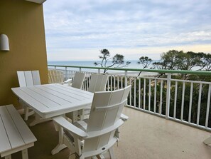 A balcony with white chairs and a table, overlooking a beach with trees and the ocean. - Luxury Oceanfront Penthouse w/ Ocean Views (Hilton Head Island)