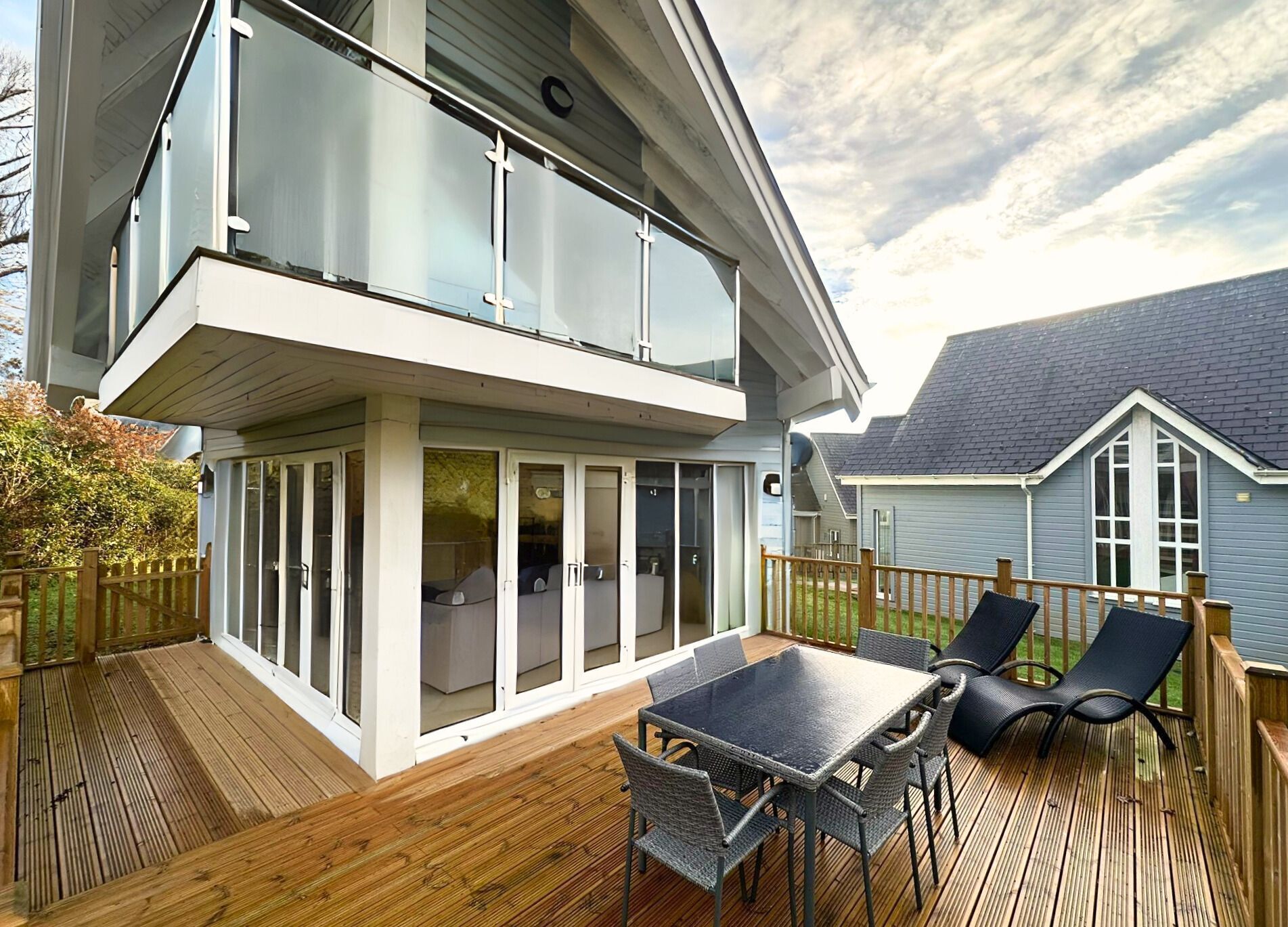 A modern two-story house with a deck, outdoor seating, and a large windowed area.