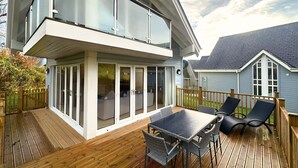 Una casa moderna de dos pisos con una terraza, mobiliario exterior y un amplio ventanal.