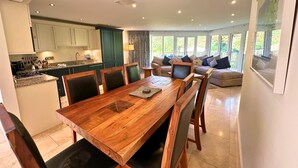 Una cocina amplia con electrodomésticos modernos, un comedor con mesa y sillas de madera, y una zona de estar acogedora con sofá y cojines.