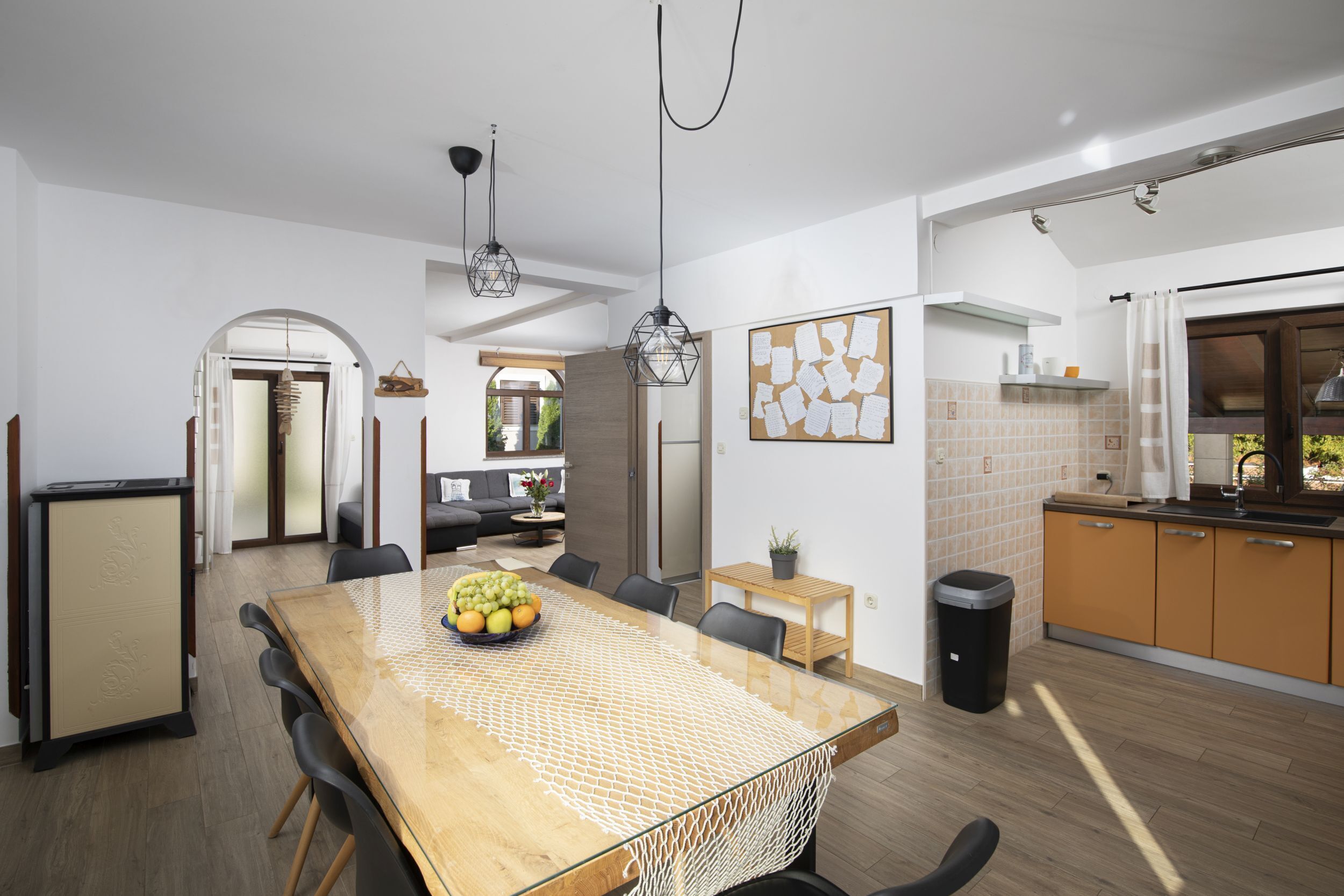 A modern kitchen with wooden cabinets, a dining area with a glass table, and a visible trash bin.