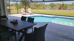 A pool area with a table and chairs, a grill, and a view of a lake and trees. - 3 bed/3 bath with Stunning Lakeview from private pool (Rotonda West)