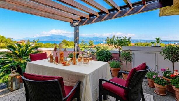 A terrace with a table set for dining, surrounded by potted plants and wicker chairs.