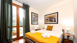 A hotel room with a bed, two bedside tables, a window with curtains, and two framed artworks on the wall.