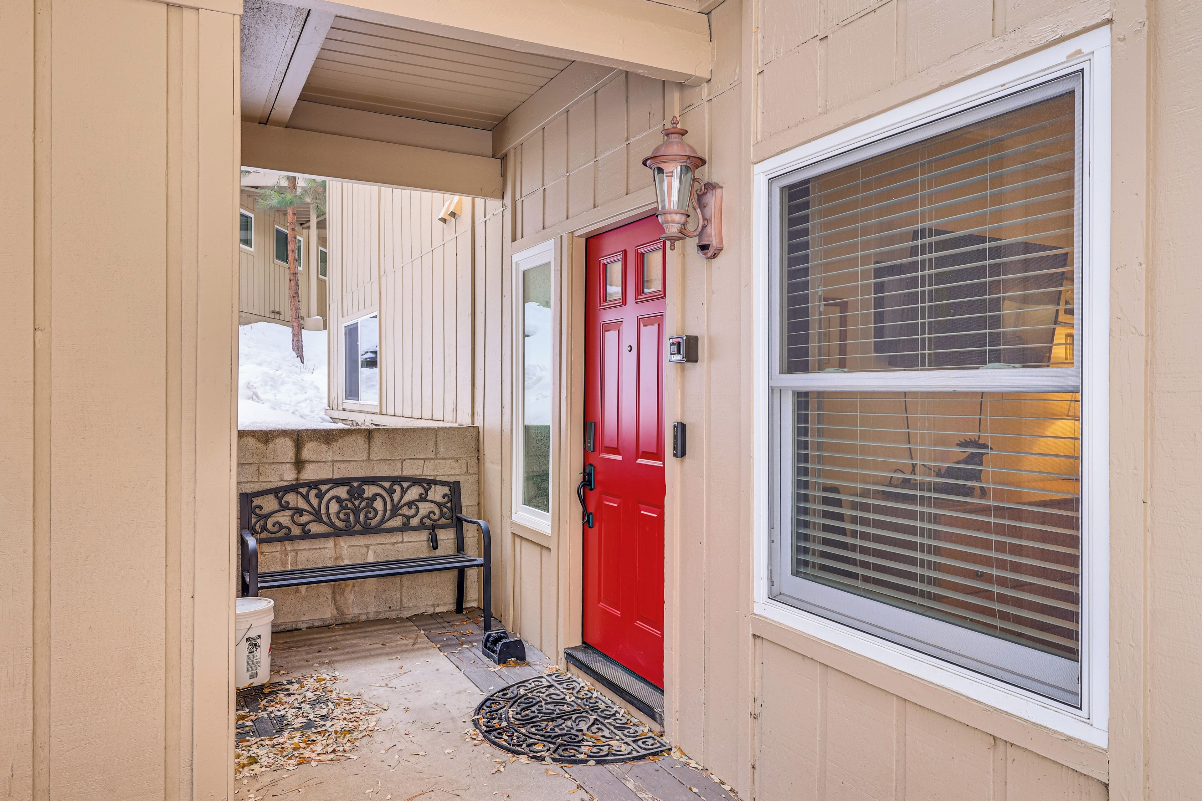 A red door with a mailbox, a bench, and a window with blinds.