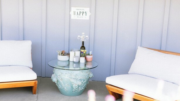 Una habitación con dos sofás blancos, una mesa de centro de cristal con motivos florales y un letrero que dice 'THIS IS OUR HAPPY PLACE'.