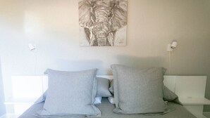 Un dormitorio con una cama, dos almohadas, una obra de arte colgada en la pared de un elefante y una mesita de noche blanca.