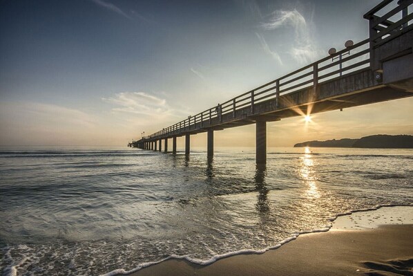 Un muelle se adentra en aguas tranquilas con un atardecer al fondo.