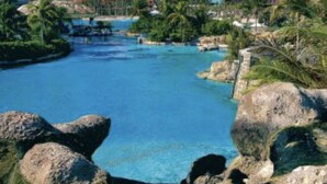 A resort with a large pool, palm trees, and a prominent building with an archway in the background. - Vacation Rental Villa sleeps 4;Harborside Resort at Atlantis, Bahamas; Dec16-21 (Paradise Island)