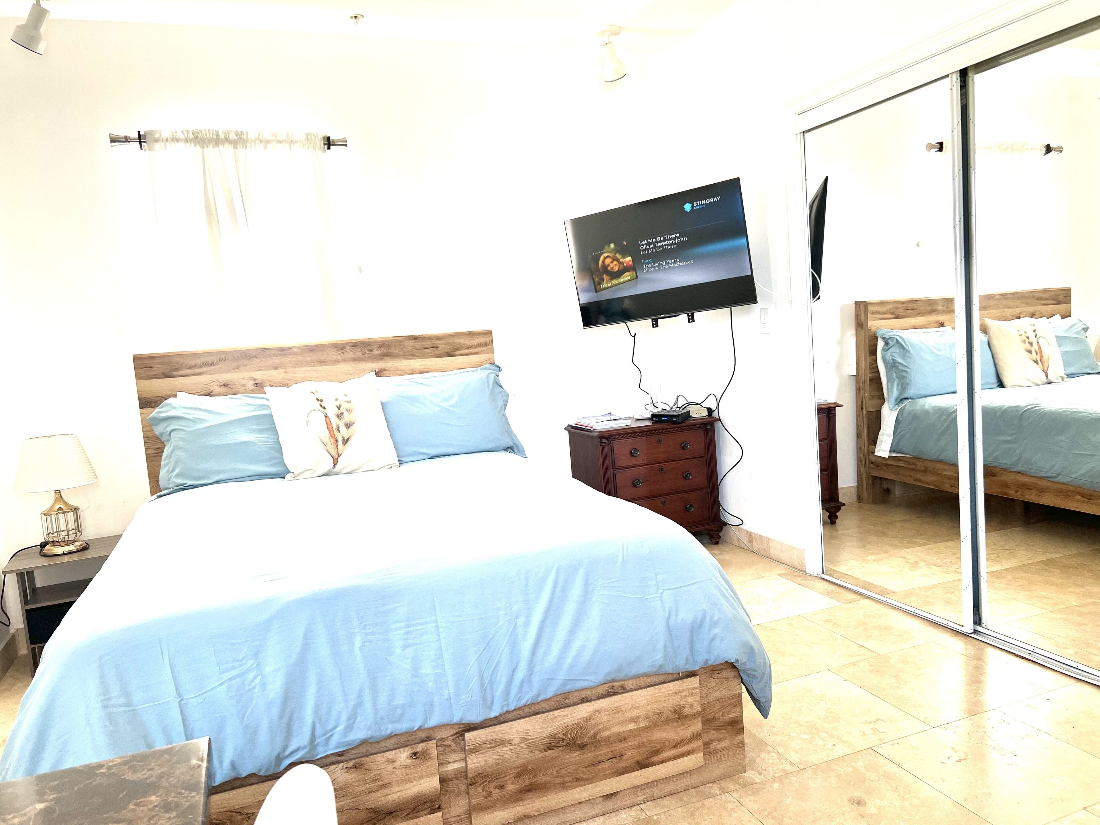 Un dormitorio con una cama de madera, un televisor montado en la pared, una mesita de noche y un aparador.