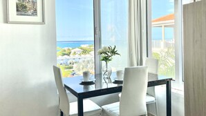 Un coin repas avec une table et des chaises, un tableau encadré au mur et une vue sur l’océan par de grandes fenêtres.