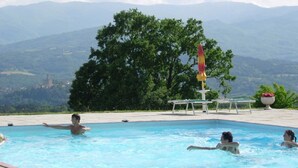 Ein Schwimmbecken mit Personen, umgeben von einer Berg- und Baumlandschaft.