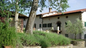 Ein Gebäude mit Steinmauern, einem Ziegeldach, einem Balkon und einer kleinen Gartenanlage mit Rasen und Sträuchern.