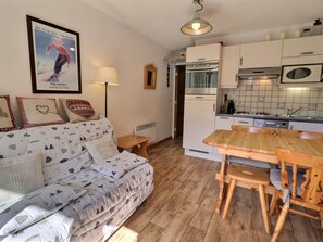 Un salon chaleureux avec un canapé, une table à manger en bois et un coin cuisine équipé d’appareils électroménagers.