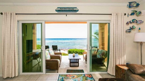 A living room with a view of the ocean, furnished with wicker chairs and a coffee table. - Mahogany Point 5: 3 BR / 3 BA villa in North Side, Sleeps 6 (KY1-1007)