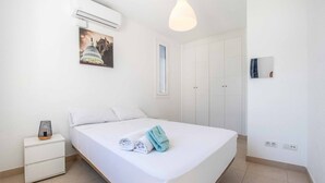 Een net opgemaakt bed met handdoeken, een bedlamp en een wandairconditioner.