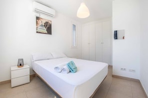 Een net opgemaakt bed met handdoeken, een bedlamp en een wandairconditioner.