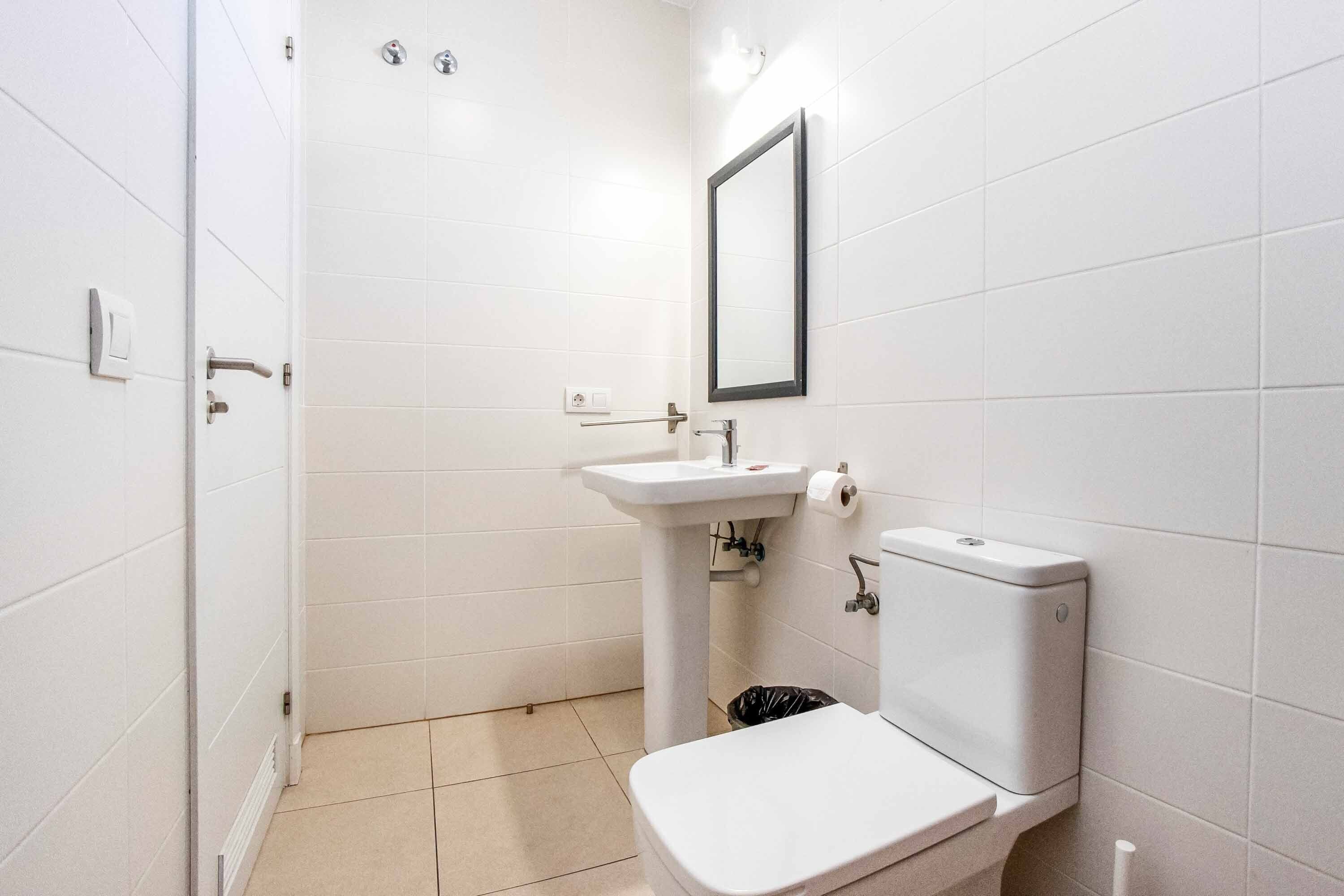 Une petite salle de bain propre, avec des carreaux blancs, un lavabo, des toilettes et un miroir.