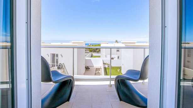 Een balkon met twee zwarte stoelen, een glazen deur en uitzicht op een gebouw en de zee.