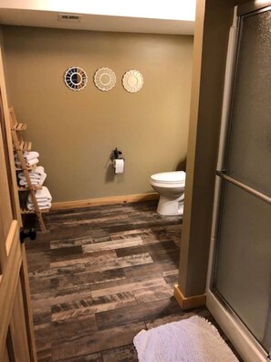 A bathroom with a wooden floor, a toilet, and a towel rack with folded towels.
